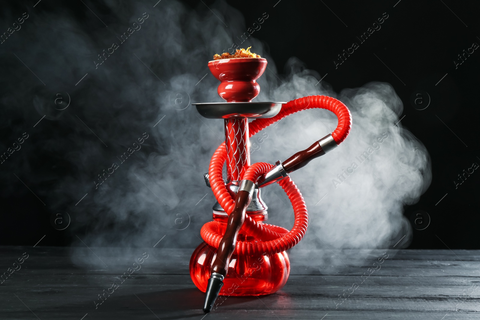 Hookah on wooden table with smoke against black background Photo of Hookah on wooden table with smoke against black background