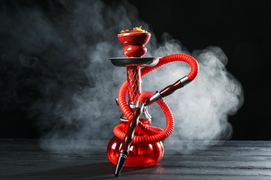Photo of Hookah on wooden table with smoke against black background
