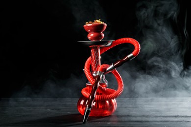 Photo of Hookah on wooden table with smoke against black background