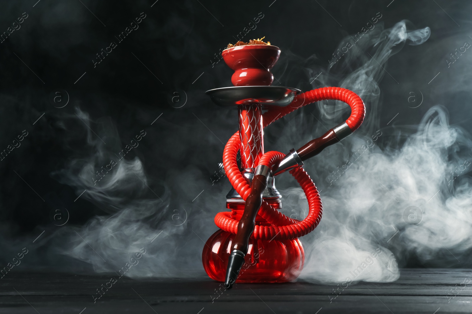 Hookah on wooden table with smoke against black background Photo of Hookah on wooden table with smoke against black background