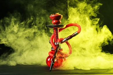 Photo of Hookah on wooden table with smoke in color lights against black background