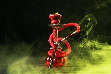 Photo of Hookah on wooden table with smoke in color lights against black background