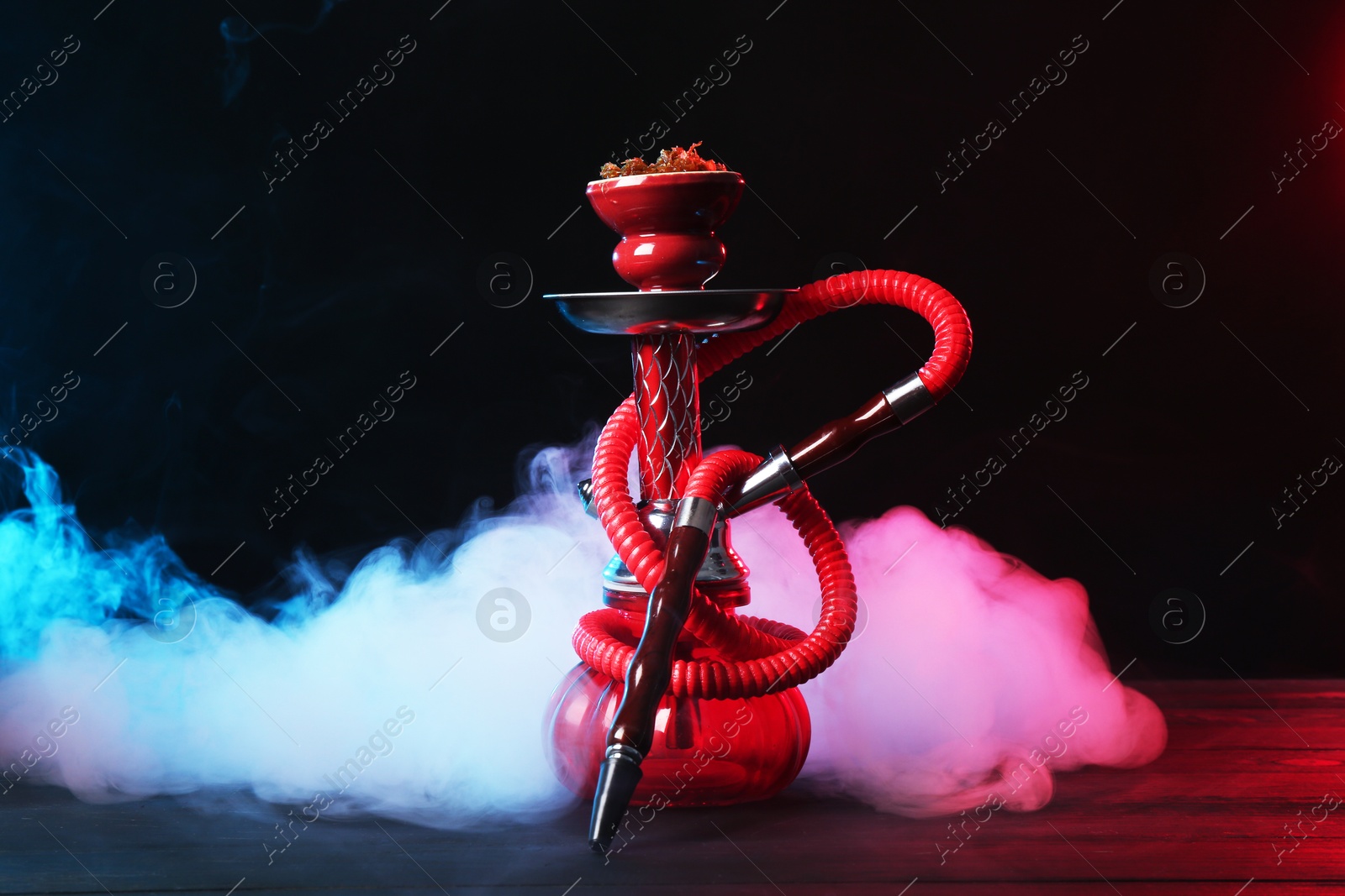 Hookah on wooden table with smoke in color lights against black background Photo of Hookah on wooden table with smoke in color lights against black background