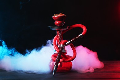 Photo of Hookah on wooden table with smoke in color lights against black background