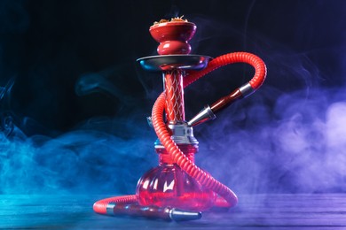 Photo of Hookah on wooden table with smoke in color lights against black background