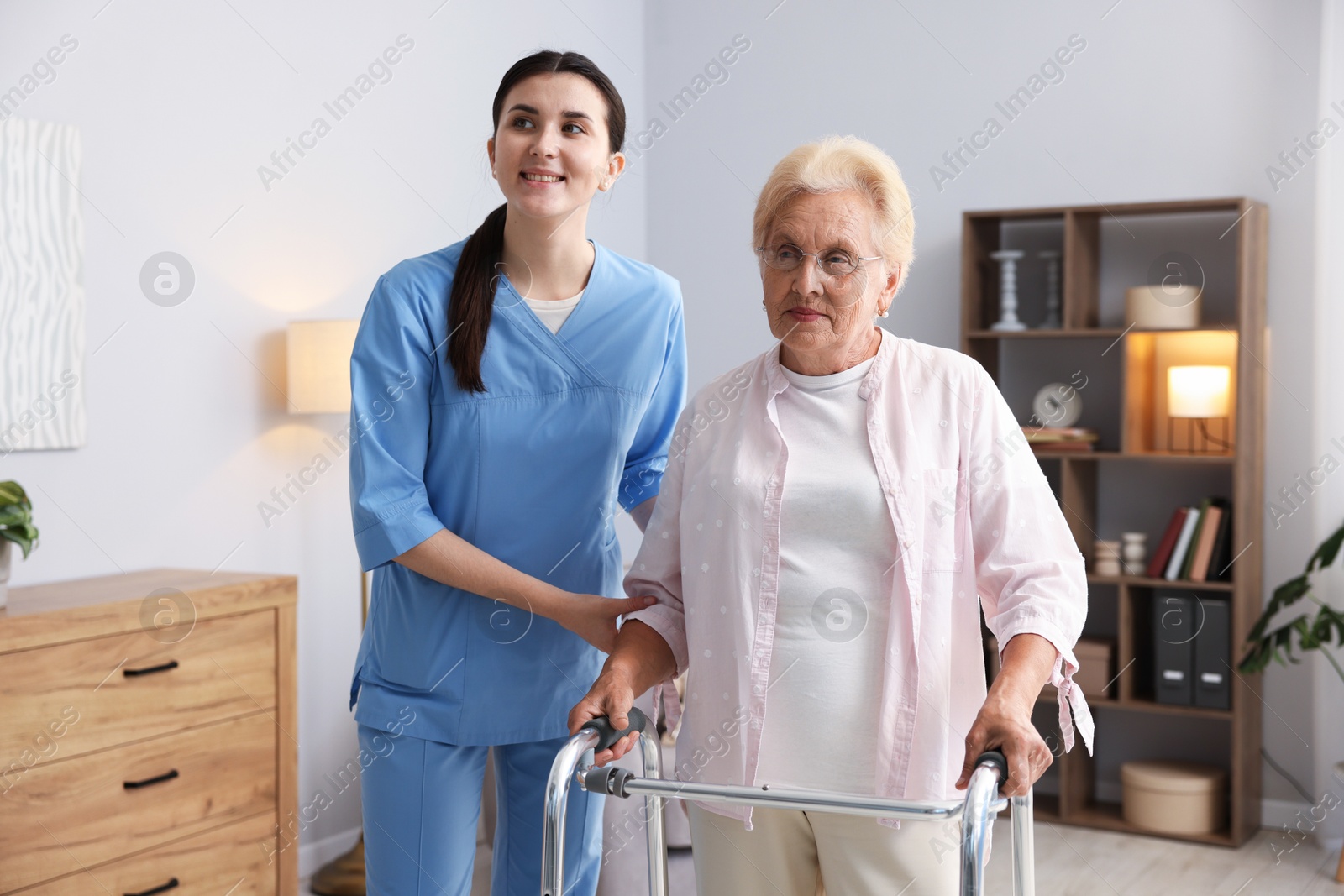 Nurse assisting senior woman with walking frame indoors. Home health care service Photo of Nurse assisting senior woman with walking frame indoors. Home health care service