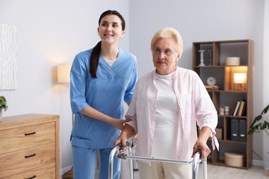 Photo of Nurse assisting senior woman with walking frame indoors. Home health care service