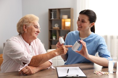 Photo of Nurse giving pills to senior woman at wooden table indoors. Home health care service