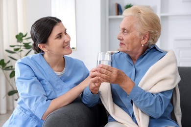 Photo of Nurse giving glass of water to senior woman indoors. Home health care service