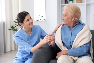 Photo of Nurse giving glass of water to senior woman indoors. Home health care service