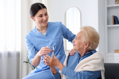 Photo of Nurse giving glass of water to senior woman indoors. Home health care service