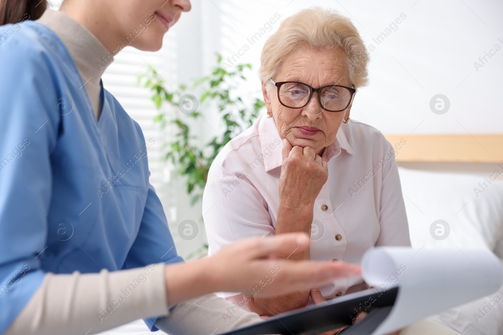 Nurse with clipboard examining senior woman indoors, closeup. Home health care service Photo of Nurse with clipboard examining senior woman indoors, closeup. Home health care service