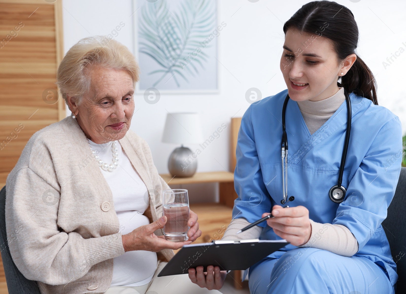 Nurse with clipboard examining senior woman indoors. Home health care service Photo of Nurse with clipboard examining senior woman indoors. Home health care service