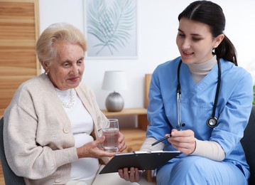 Photo of Nurse with clipboard examining senior woman indoors. Home health care service