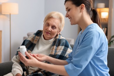 Photo of Nurse giving water to senior woman on sofa indoors. Home health care service