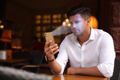 Image of Man unlocking his smartphone with facial recognition app in cafe. Biometric verification