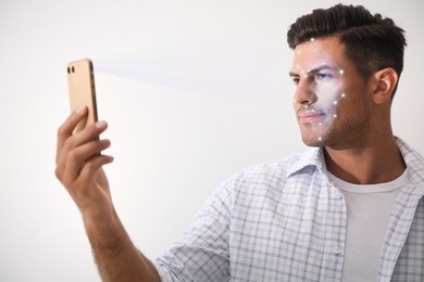 Image of Man unlocking his smartphone with facial scanner against light background. Biometric verification