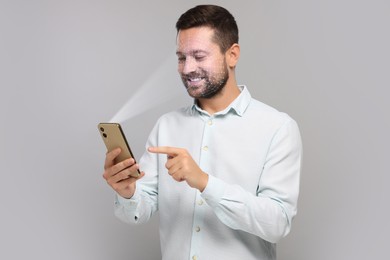 Image of Man unlocking his smartphone with facial recognition app against light grey background. Biometric verification
