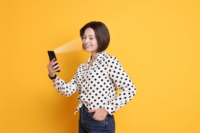 Image of Woman unlocking her smartphone with facial scanner against orange background. Biometric verification