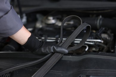 Photo of Auto part. Professional mechanic with timing belt near open hood of car indoors, closeup