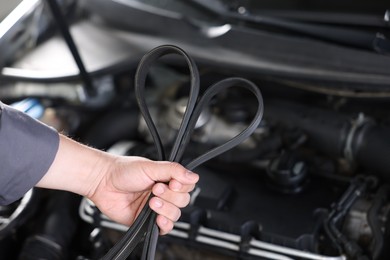 Photo of Auto part. Professional mechanic with timing belt near open hood of car indoors, closeup