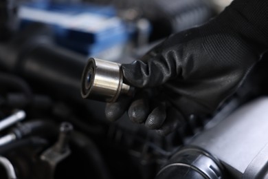 Photo of Auto part. Professional mechanic with bearings near open hood of car indoors, closeup