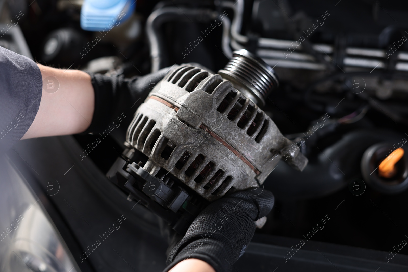 Auto part. Professional mechanic with alternator near open hood of car indoors, above view Photo of Auto part. Professional mechanic with alternator near open hood of car indoors, above view