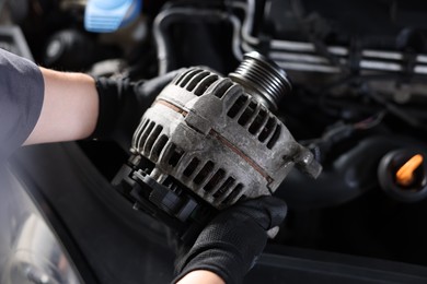 Photo of Auto part. Professional mechanic with alternator near open hood of car indoors, above view
