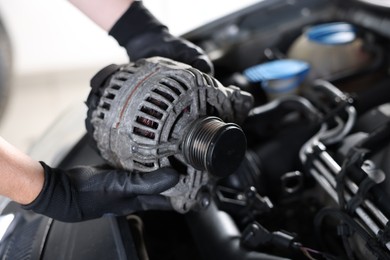 Photo of Auto part. Professional mechanic with alternator near open hood of car indoors, closeup