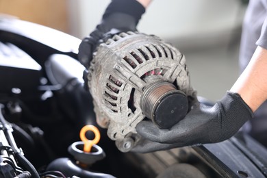 Photo of Auto part. Professional mechanic with alternator near open hood of car indoors, closeup