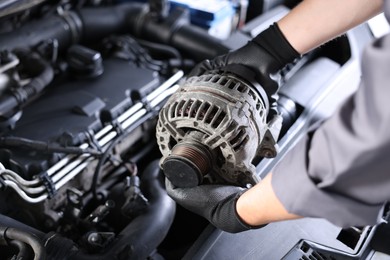 Photo of Auto part. Professional mechanic with alternator near open hood of car indoors, closeup