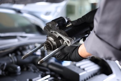 Photo of Auto part. Professional mechanic with starter motor near open hood of car indoors, closeup