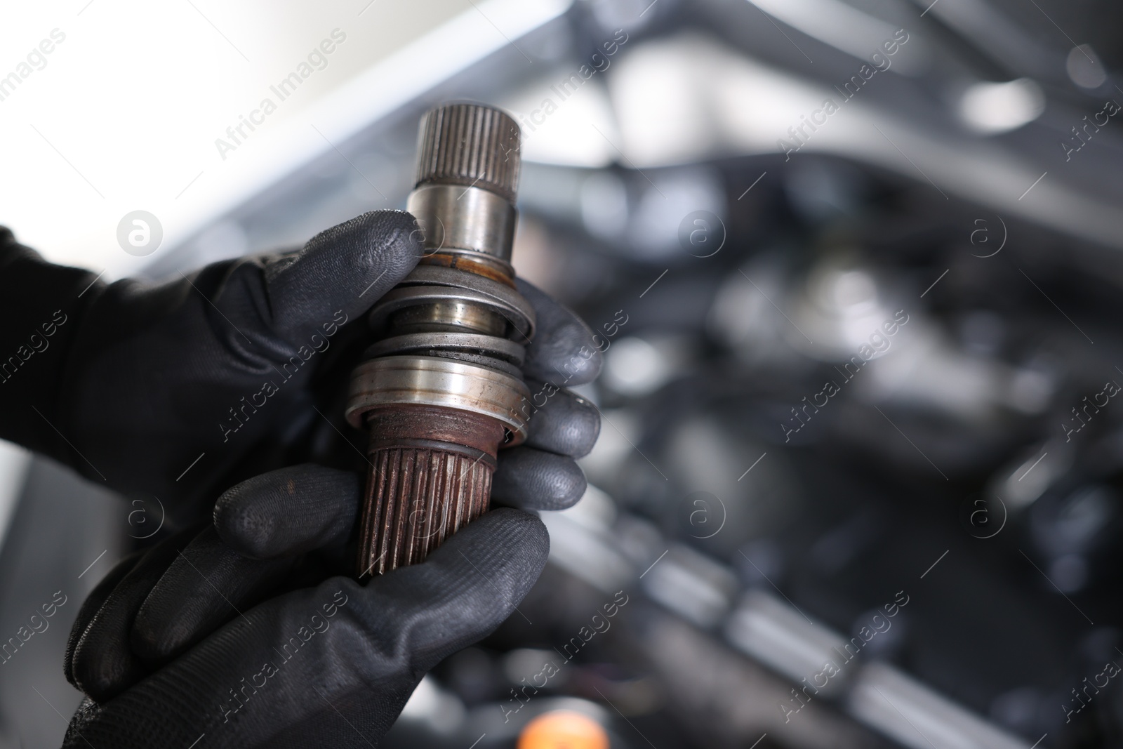 Auto part. Professional mechanic with drive shaft near open hood of car indoors, closeup. Space for text Photo of Auto part. Professional mechanic with drive shaft near open hood of car indoors, closeup. Space for text