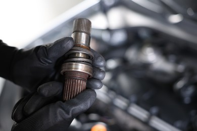 Photo of Auto part. Professional mechanic with drive shaft near open hood of car indoors, closeup. Space for text