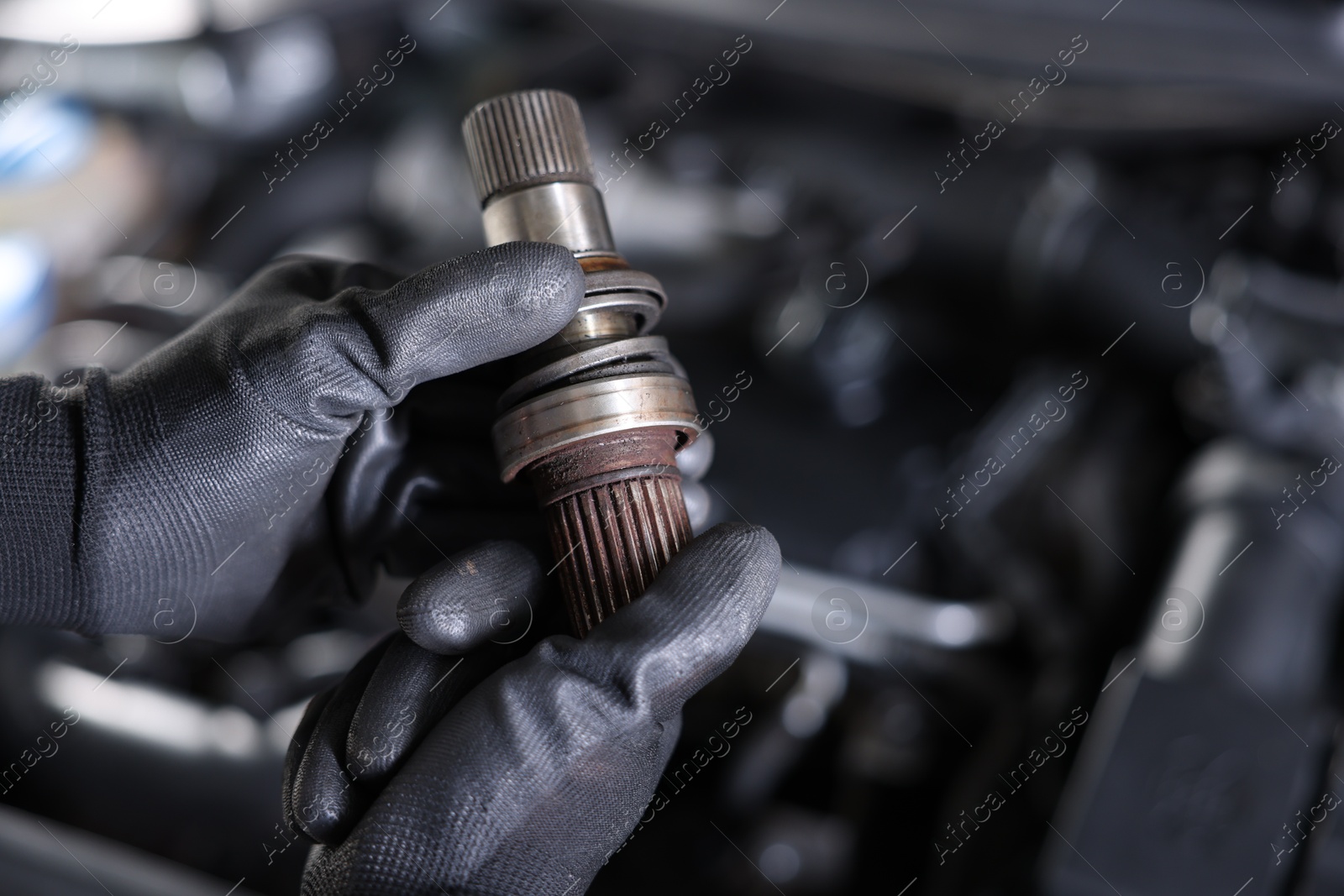 Auto part. Professional mechanic with drive shaft near open hood of car indoors, closeup. Space for text Photo of Auto part. Professional mechanic with drive shaft near open hood of car indoors, closeup. Space for text
