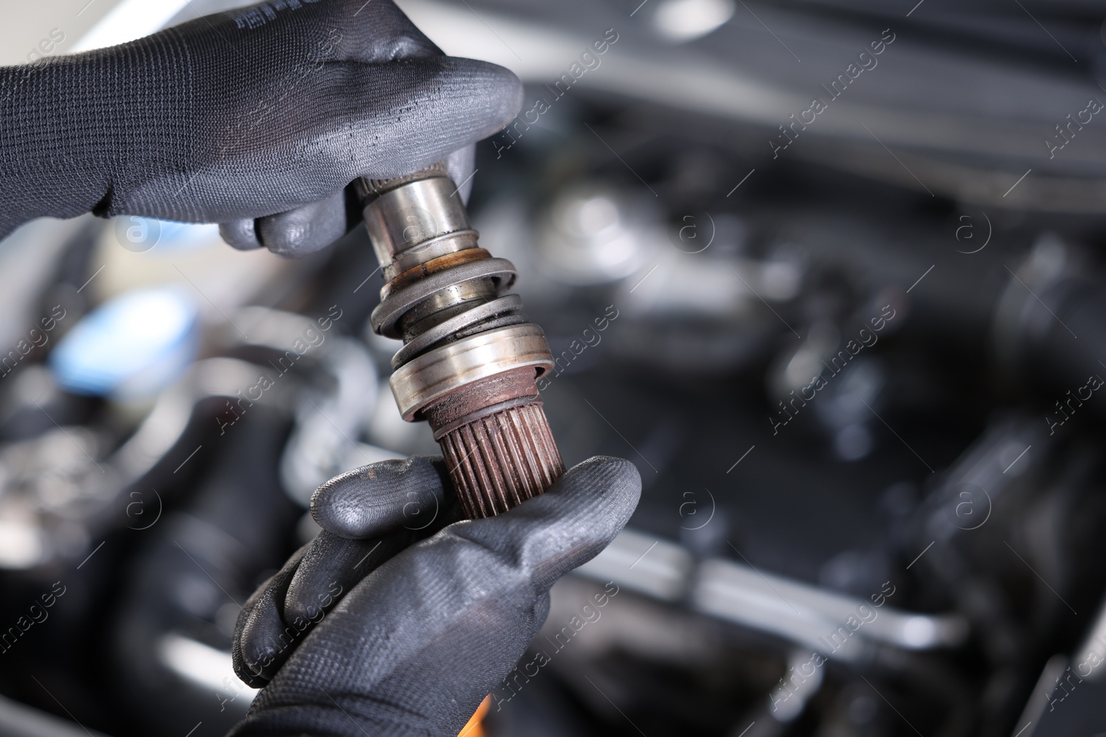Auto part. Professional mechanic with drive shaft near open hood of car indoors, closeup. Space for text Photo of Auto part. Professional mechanic with drive shaft near open hood of car indoors, closeup. Space for text