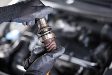 Photo of Auto part. Professional mechanic with drive shaft near open hood of car indoors, closeup. Space for text