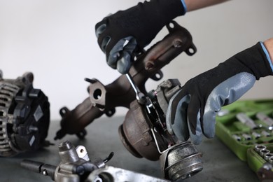 Photo of Auto parts. Professional mechanic with wrench fixing turbocharger at table indoors, closeup