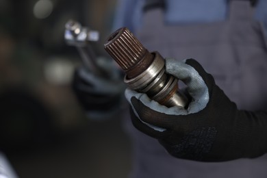 Photo of Auto part. Professional mechanic with drive shaft and tool indoors, closeup. Space for text