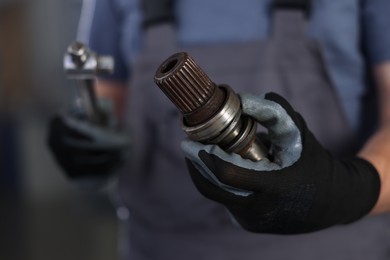 Photo of Auto part. Professional mechanic with drive shaft and tool indoors, closeup