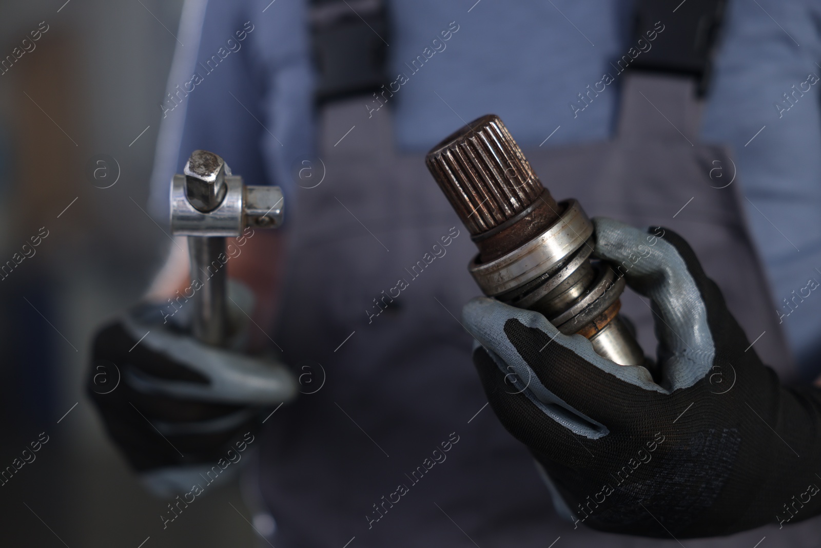 Auto part. Professional mechanic with drive shaft and tool indoors, closeup Photo of Auto part. Professional mechanic with drive shaft and tool indoors, closeup