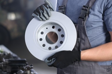 Photo of Auto parts. Professional mechanic with brake disc indoors, closeup