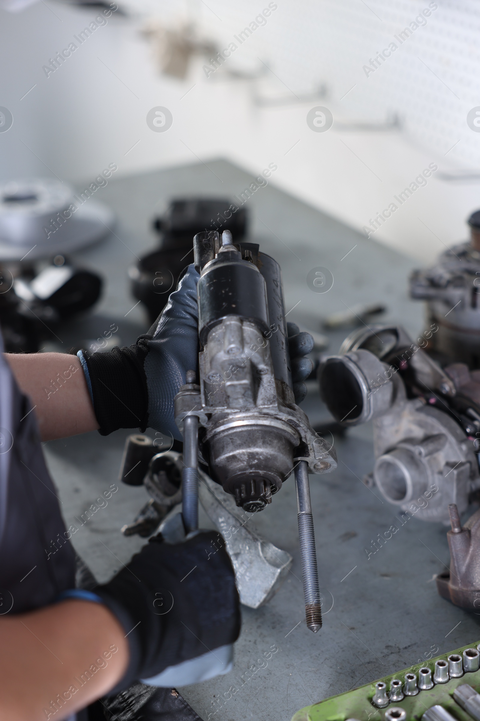 Auto parts. Professional mechanic with starter motor at grey table indoors, closeup Photo of Auto parts. Professional mechanic with starter motor at grey table indoors, closeup