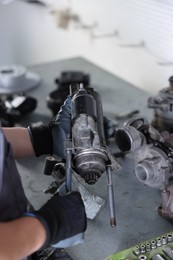 Photo of Auto parts. Professional mechanic with starter motor at grey table indoors, closeup