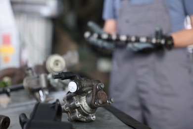 Photo of Professional mechanic with camshaft indoors, focus on different auto parts