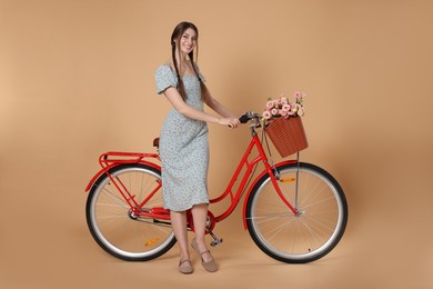 Photo of Smiling woman in dress and bicycle with basket of flowers on beige background