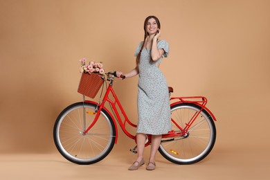 Photo of Smiling woman in dress and bicycle with basket of flowers on beige background