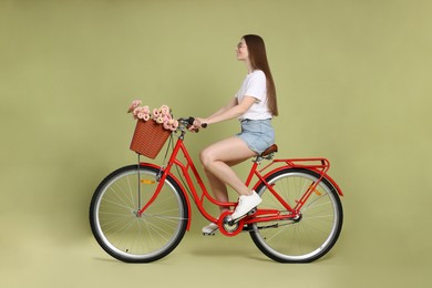 Photo of Smiling woman in sunglasses riding bicycle with basket of flowers on green background
