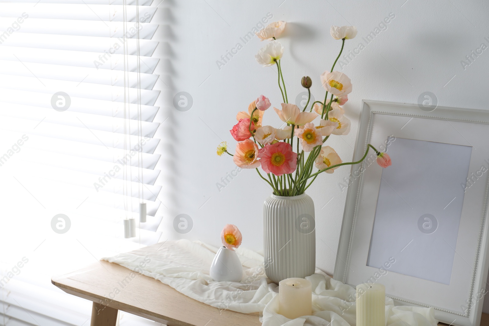 Photo of Bouquet of beautiful poppy flowers, frame and burning candles on table indoors. Space for text