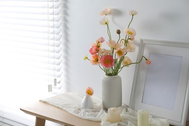 Photo of Bouquet of beautiful poppy flowers, frame and burning candles on table indoors. Space for text